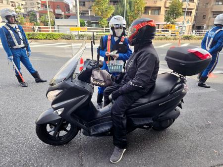 バイク利用者に交通事故への注意を促す警察官＝１８日午前、東京都江戸川区