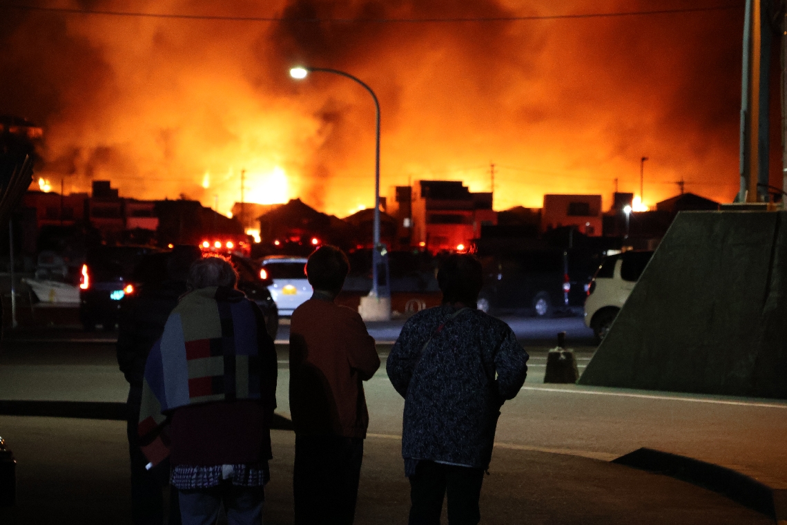 燃える家並みを不安そうに見つめる地元住民ら＝１８日午後８時１６分