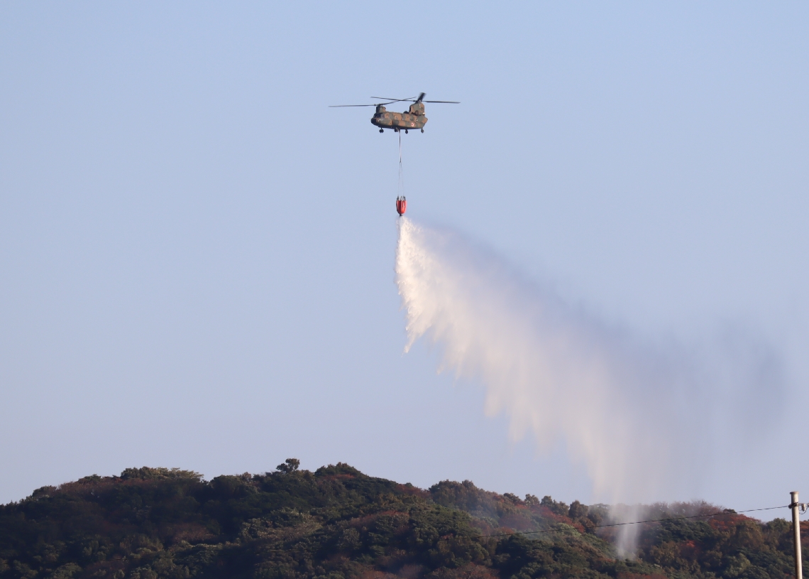 煙が上がる蔦島に上空から放水する自衛隊のヘリコプター＝２１日、大分市佐賀関