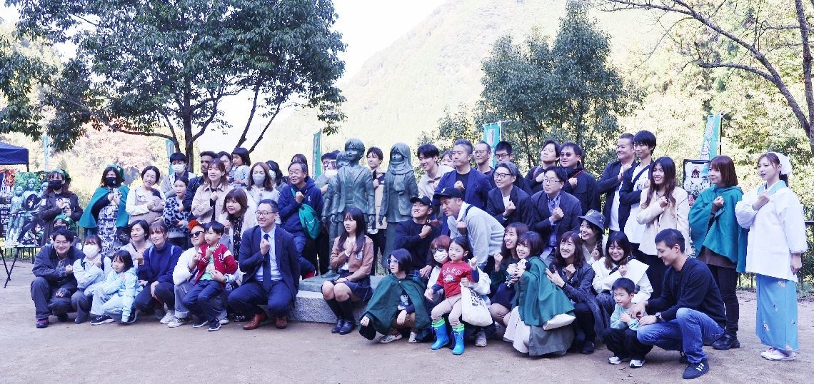 作品ゆかりの大山ダムに集った「進撃の日田まちおこし協議会」のメンバーやファンら＝日田市大山町