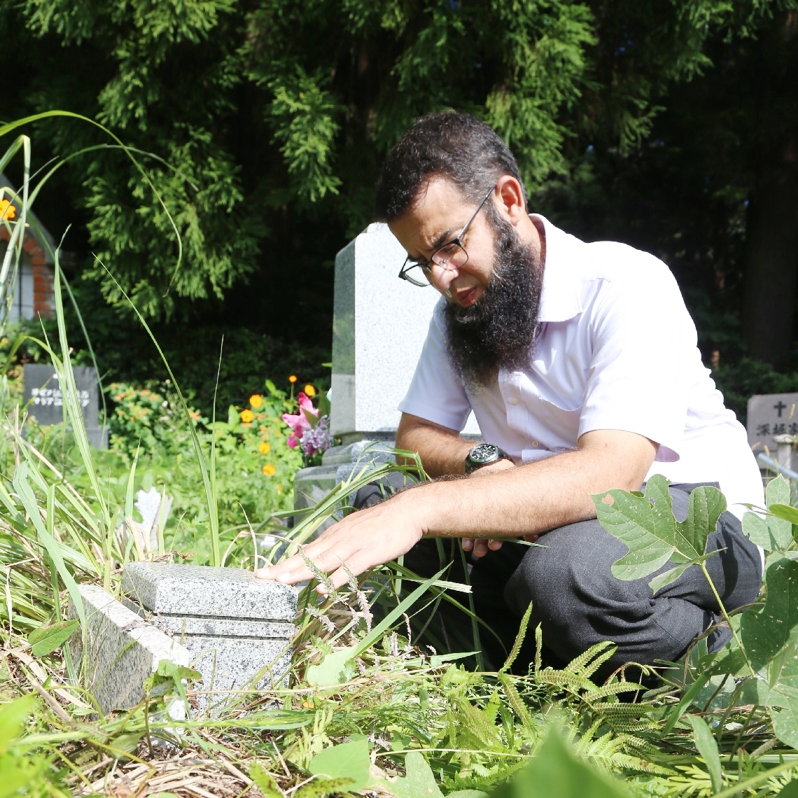 ２０１１年に亡くした子どもの墓碑に触れるザファー・サイードさん＝１０月７日、別府市内のキリスト教墓地