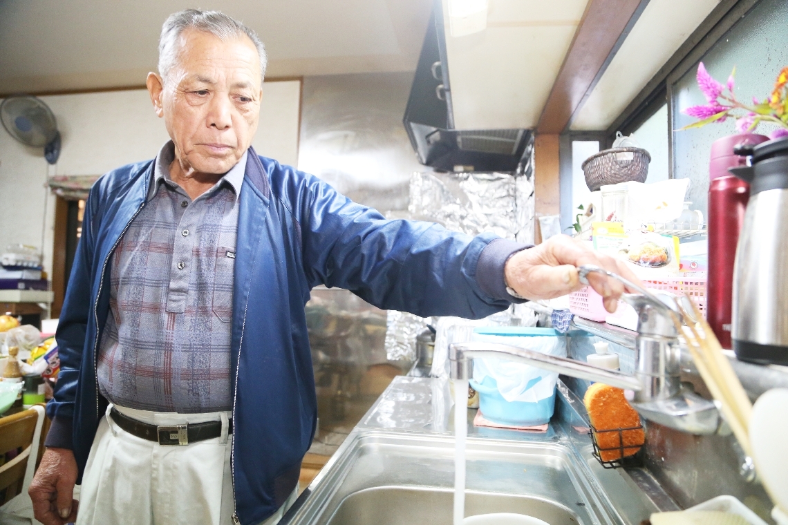 高平区の自宅で台所に立ち、蛇口の水を見つめる衛藤清隆さん＝１１月中旬、日出町南畑