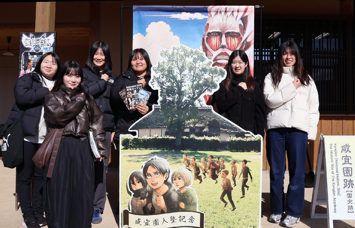 施設入り口に設置された登場人物のパネルと記念撮影する大学生＝日田市淡窓の咸宜園跡