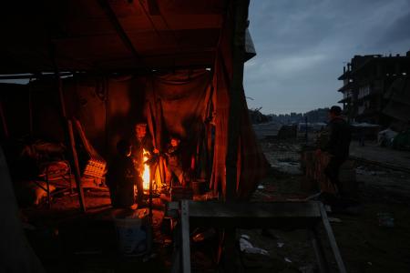 イスラエル軍の攻撃で破壊された跡で、たき火で暖をとる人たち＝１２日、ガザ（ＡＰ＝共同）
