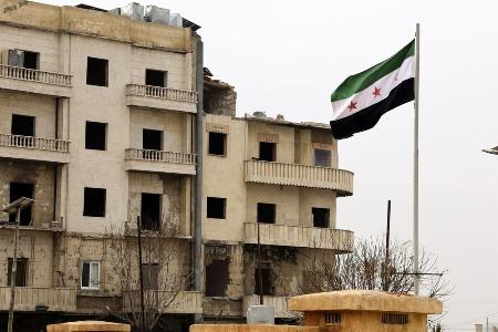 内戦で破壊された建物前に掲げられた新たなシリア国旗＝６日、北部アレッポ