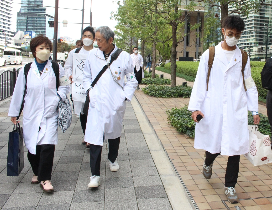大阪のオフィス街に現れた白衣の集団に足を止めて眺める人たち＝１０月、大阪市