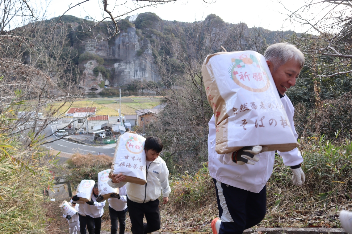 開運祈願で、そば粉の入った袋を担いで石段を上る関係者