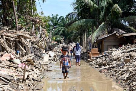 がれきが積み上がる住宅街を歩く少年＝２５日、インドネシア・クアラシンパン（共同）