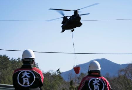 消火活動を行う陸上自衛隊のヘリコプターを見つめる地元消防団の人たち＝１８日午後、山梨県大月市