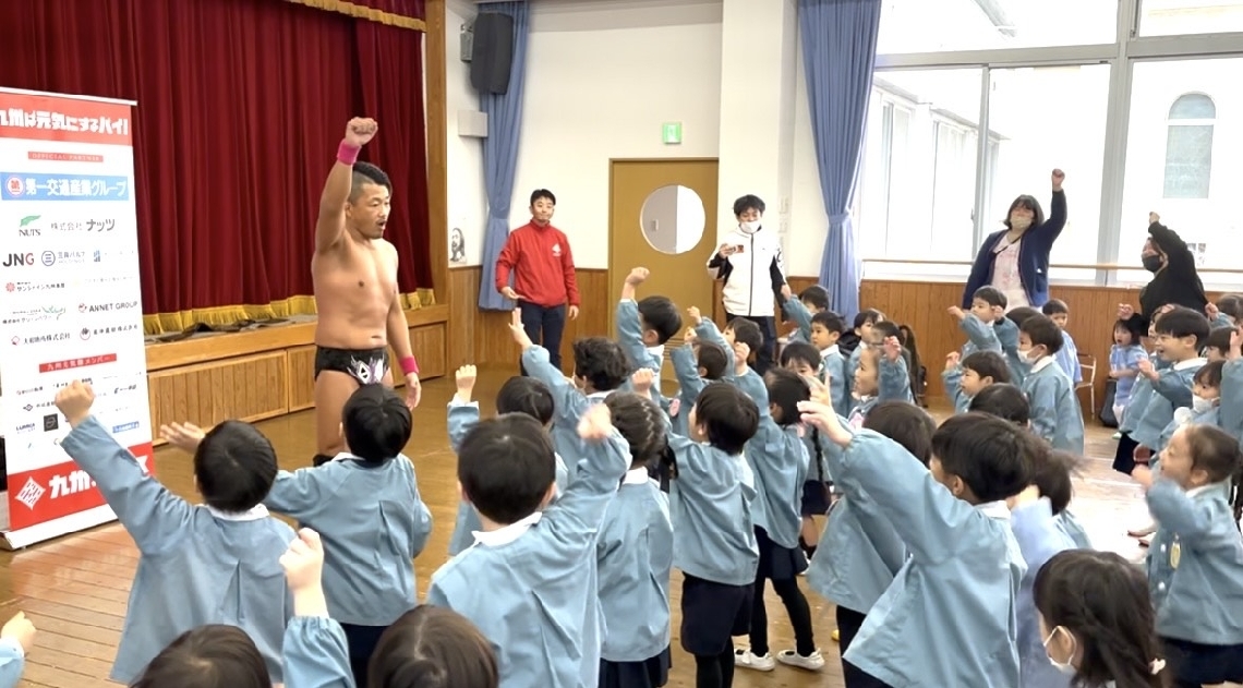 佐々木日田丸選手と一緒に元気いっぱいに拳を突き上げるカトリック海星幼稚園の園児たち