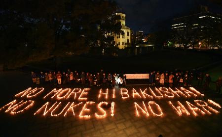 核兵器禁止条約の発効から５年を迎え、キャンドルを並べて作られた「ＮＯ　ＭＯＲＥ　ＨＩＢＡＫＵＳＨＡ」などの文字。後方は原爆ドーム＝２２日夕、広島市中区の平和記念公園