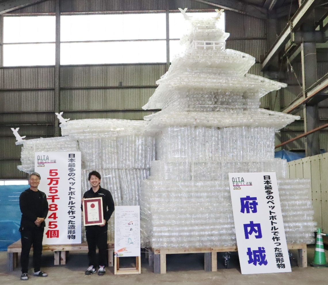 ペットボトルで作った府内城の前で認定証を持つ河野会長（右）と木野実行委員長