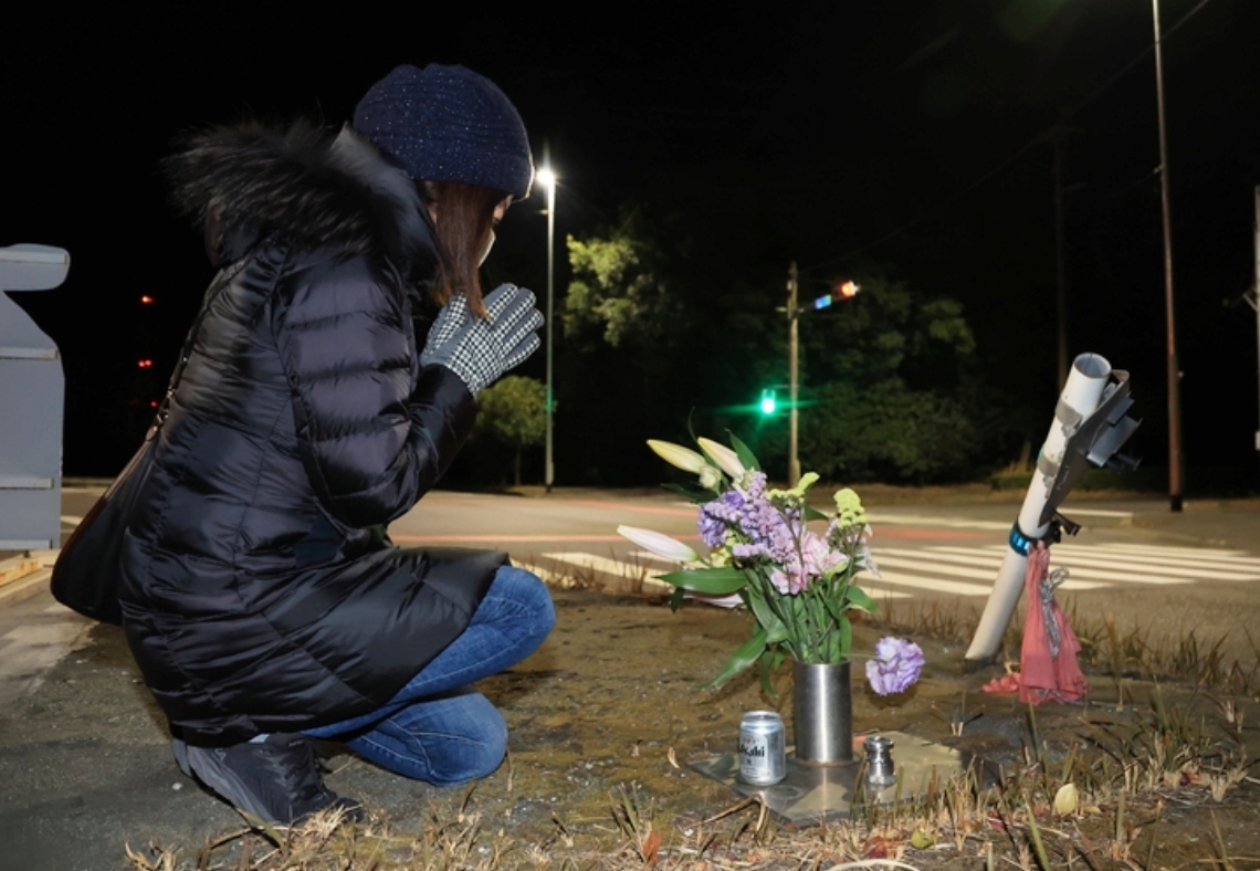 発生から５年がたった事故現場で手を合わせる遺族の長文恵さん＝９日深夜、大分市大在