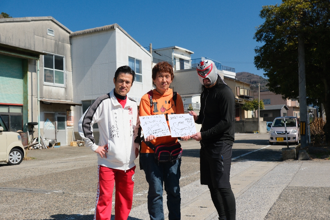 大規模火災現場付近で住民の鈴木美奈子さん（中央）にサインしたアントニオ小猪木（左）と鯖王（右）