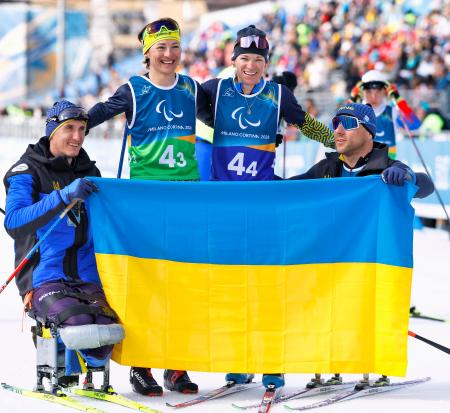 ノルディックスキー距離混合１０キロリレーで銀メダルを獲得し、国旗を掲げるオレクサンドラ・コノノワ（左から２人目）らウクライナ選手＝１４日、イタリア・テーゼロ（共同）