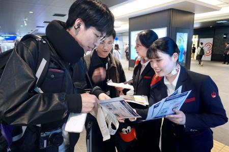 モバイルバッテリーの取り扱い変更を利用客にチラシで周知する航空会社の関係者＝１４日午後、羽田空港