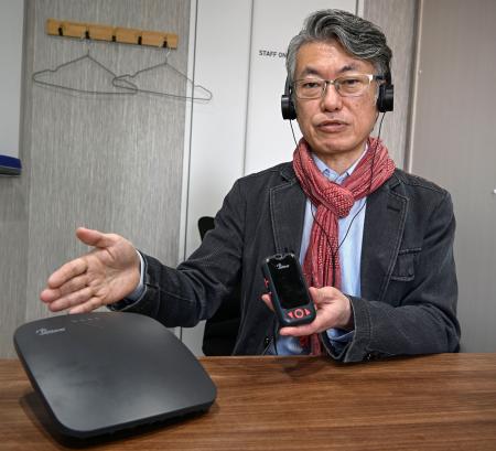 「オーラキャスト」の機器を手にする東京工科大の吉岡英樹講師＝東京都港区