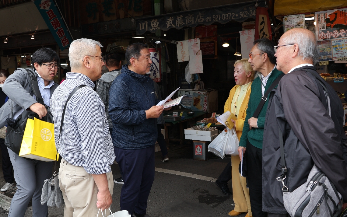 旦過市場協同組合の黒瀬善裕理事長（中央）から市場の案内を受ける臼杵市中央通り商店街振興組合の関係者