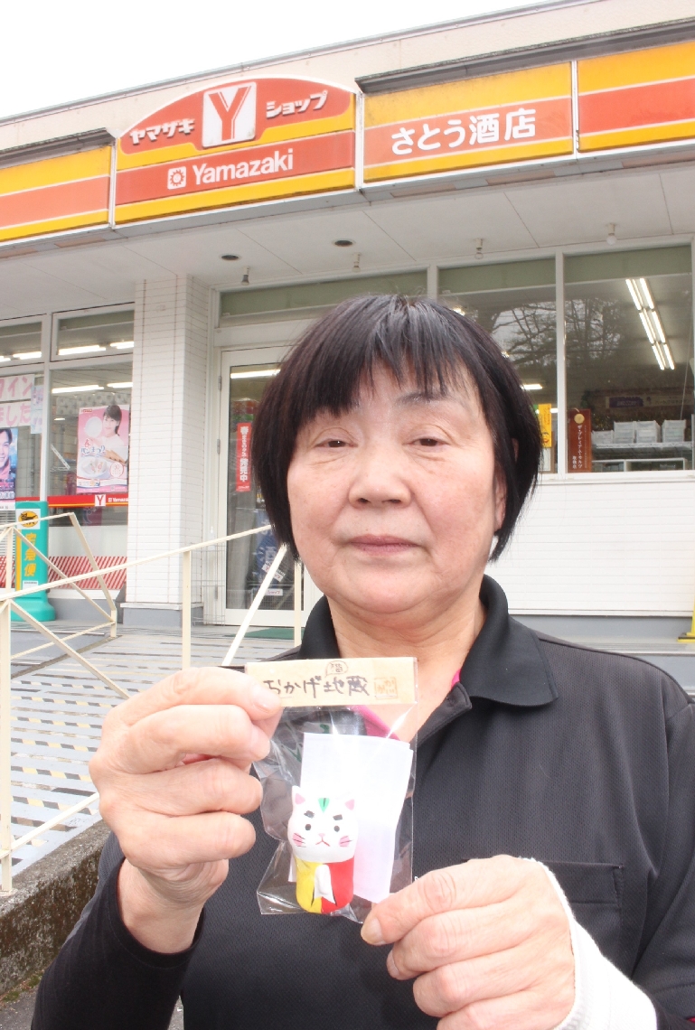 「ヤマザキショップ長湯さとう」限定の岡げ猫地蔵を持つ甲斐香代子店長