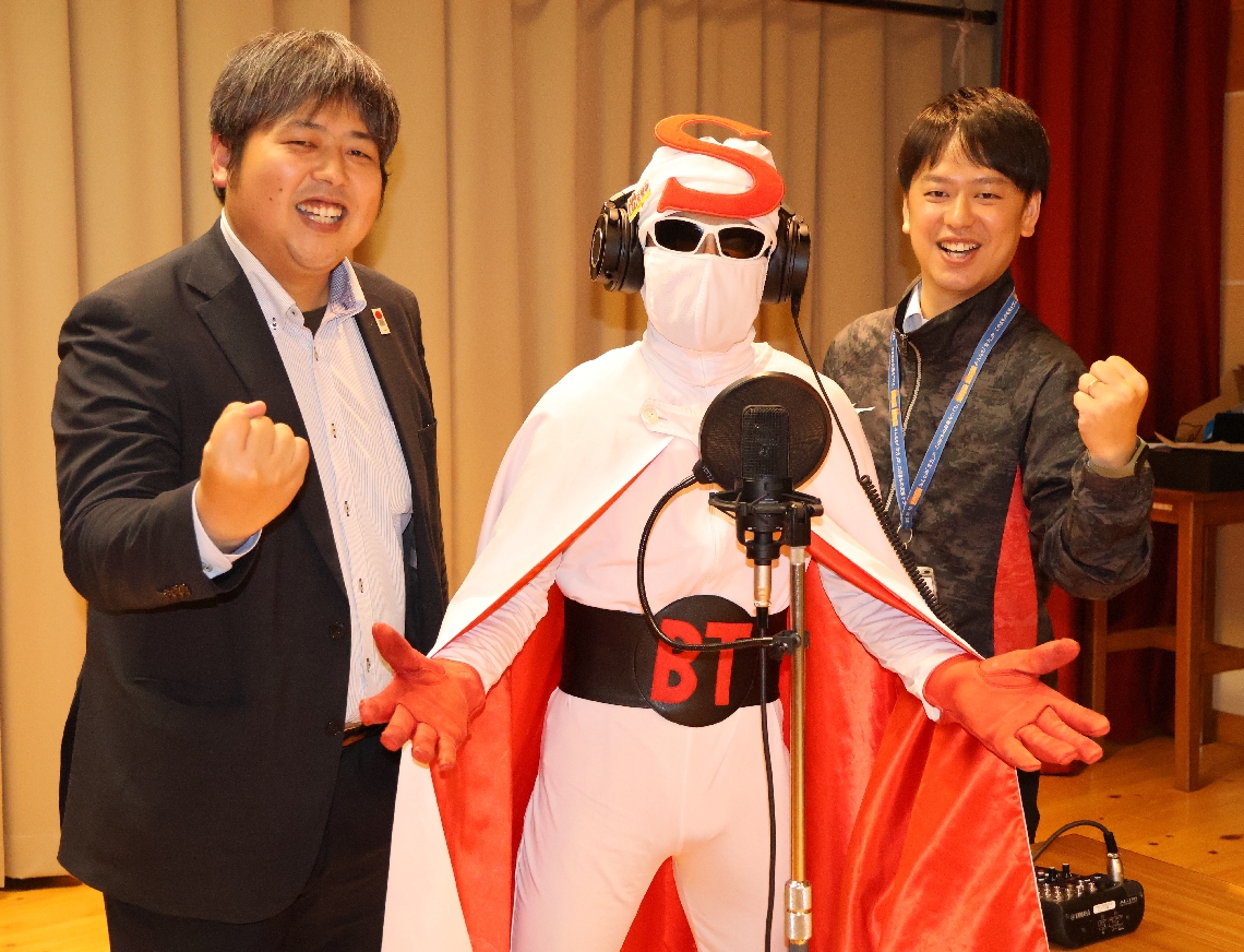マイクの前に立つ昭和仮面（中央）と、テーマソングを手がけた松本卓也さん（左）、中原幸平さん＝豊後高田市役所真玉庁舎