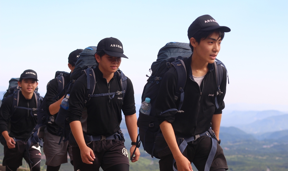 【登山縦走】仲間と協力しながら登る大分工の選手たち＝九重町田野