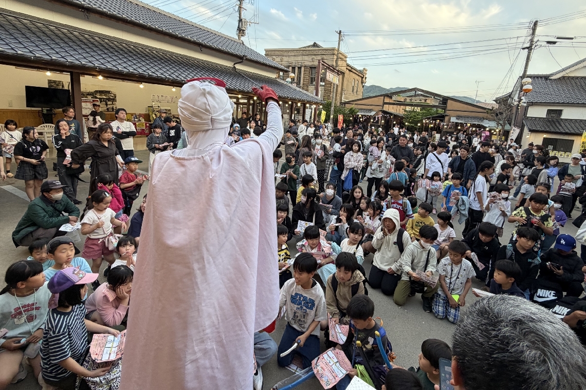 夜台市のくじ引き大会で司会をする昭和仮面＝４月２５日、豊後高田昭和の町