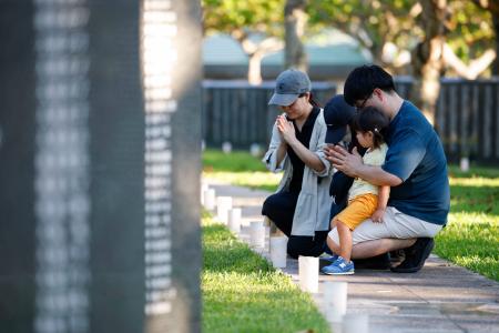 「慰霊の日」を前に、沖縄戦犠牲者の名前が刻まれた「平和の礎」に手を合わせる家族連れ＝２２日午後、沖縄県糸満市の平和祈念公園