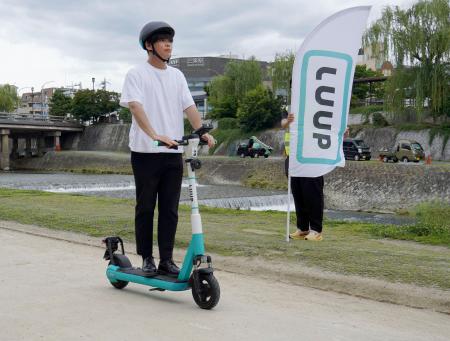鴨川沿いの河川敷を電動キックボードで走行する「Ｌｕｕｐ」の社員＝２３日午前、京都市