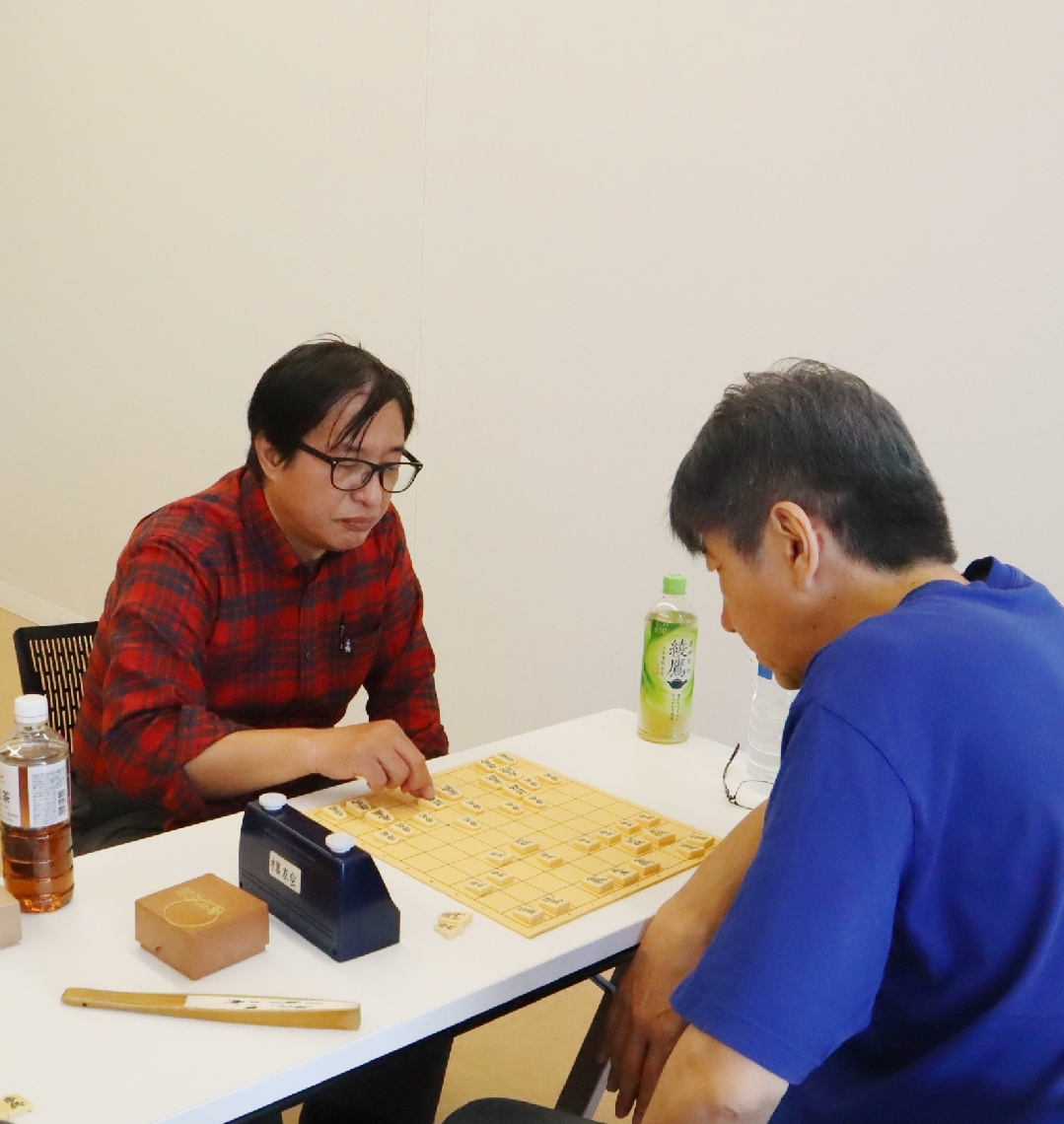 「将棋でラブ＆ピースを」と呼びかける日出町棋友会事務局の古江俊夫さん（左）