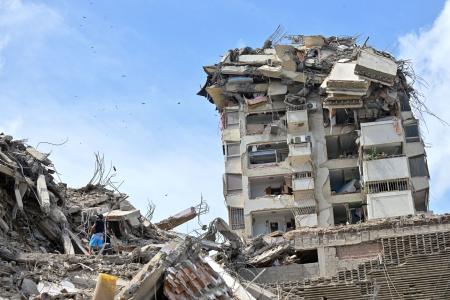 地震で崩落した建物と救出作業＝２５日、ラグアイラ（ロイター＝共同）