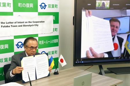 原発事故に関する知見の共有に向けた連携協定の締結式をオンラインで開き、署名した福島県双葉町の伊沢史朗町長（左）とスラブチチ市のフォミチェフ市長＝２６日午後、双葉町役場