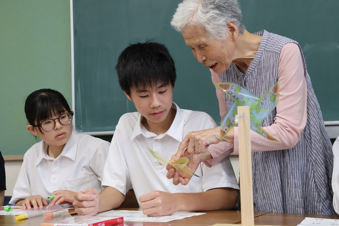 風車を中心的に制作している住民から作り方を教わる佐賀関中の生徒（左）