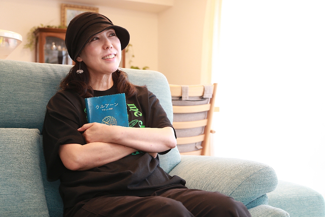 自宅ソファでイスラム教の聖典「クルアーン」を手に語る小野沢優里さん＝５月、別府市