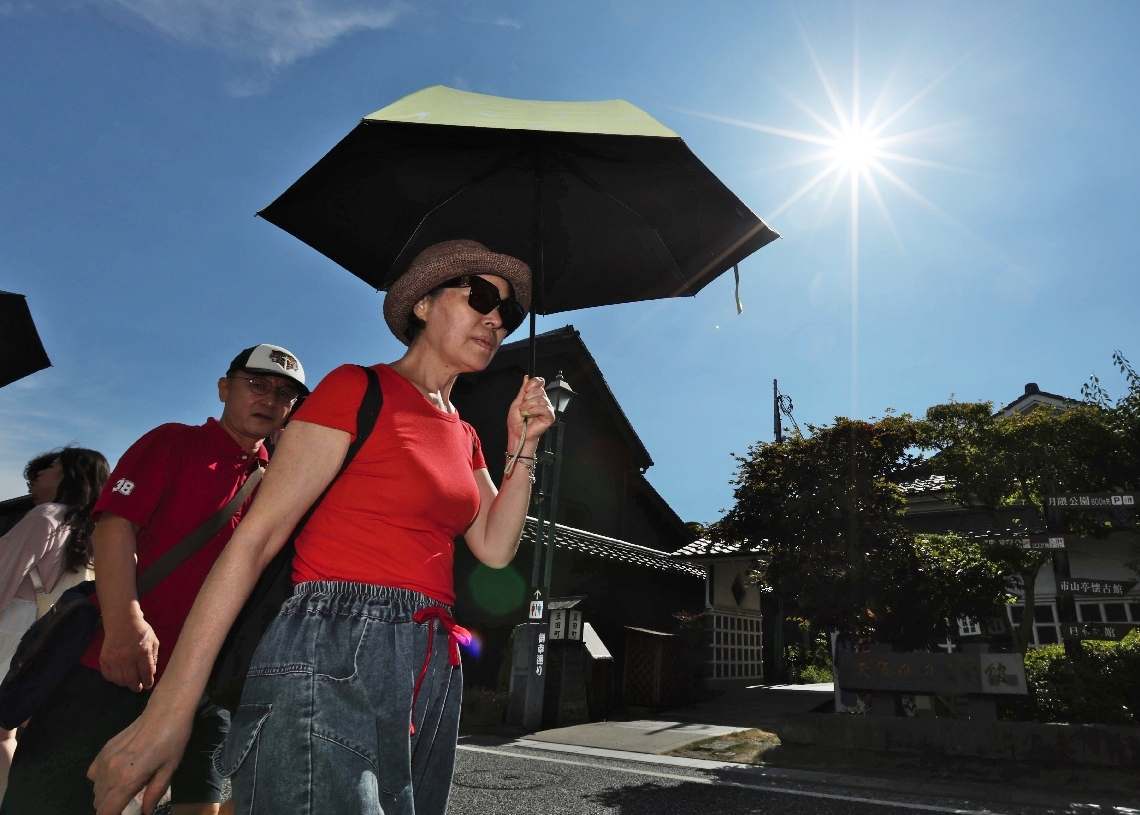 降り注ぐ太陽の下、日傘を差して歩く観光客