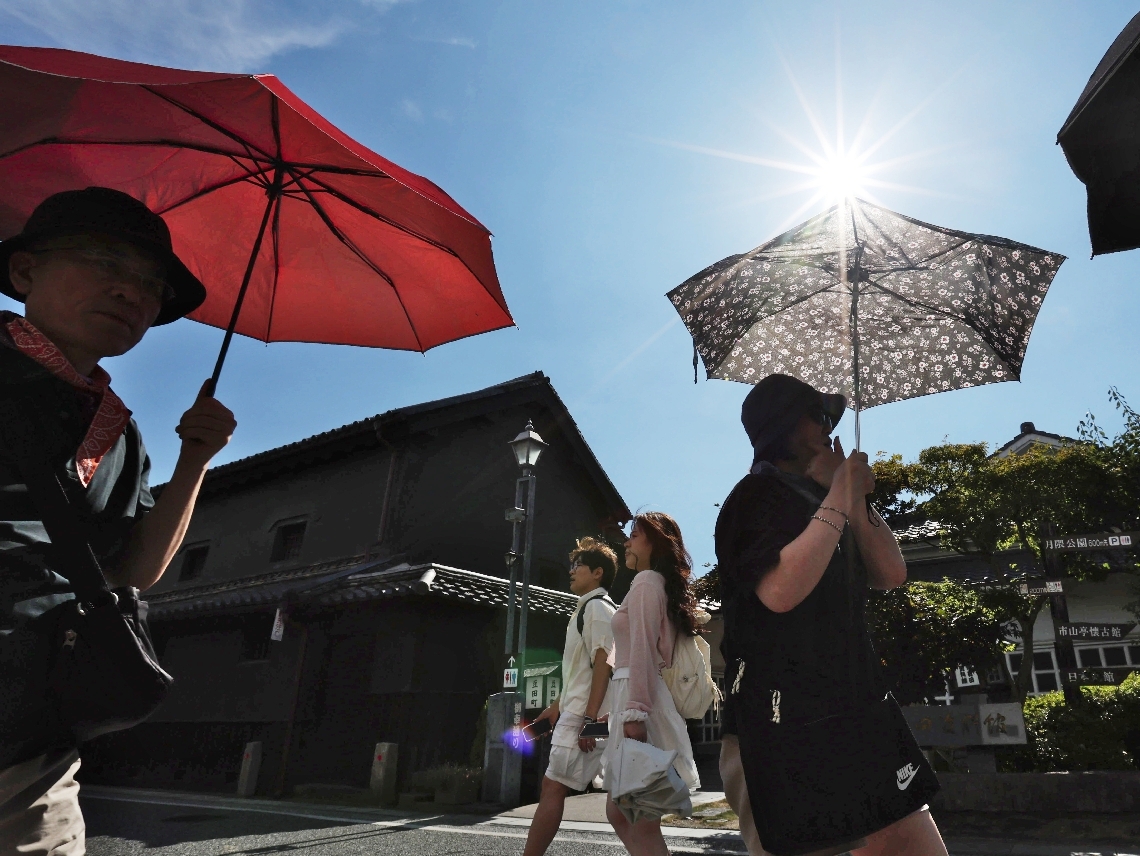 降り注ぐ太陽の下、日傘を差して歩く観光客