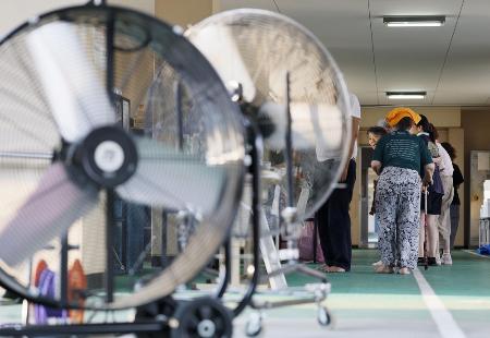 大型扇風機が稼働する熊本県氷川町の避難所で、水と食料の配給に並ぶ被災者ら＝３日
