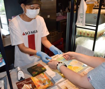 観光支援のクーポンを受け取る阿部牧場の直営販売店の従業員＝１２日、熊本県阿蘇市