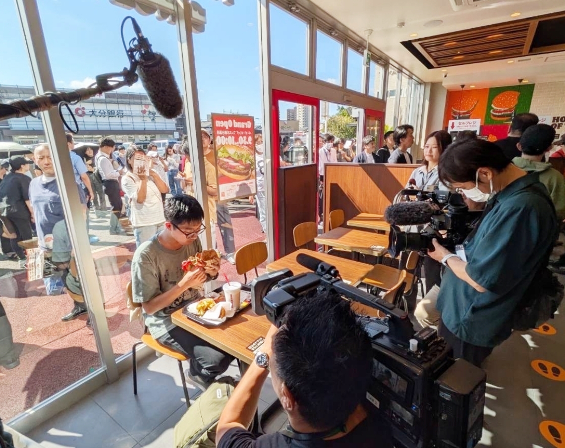 テレビカメラに囲まれワッパーを食べる筆者＝大分市